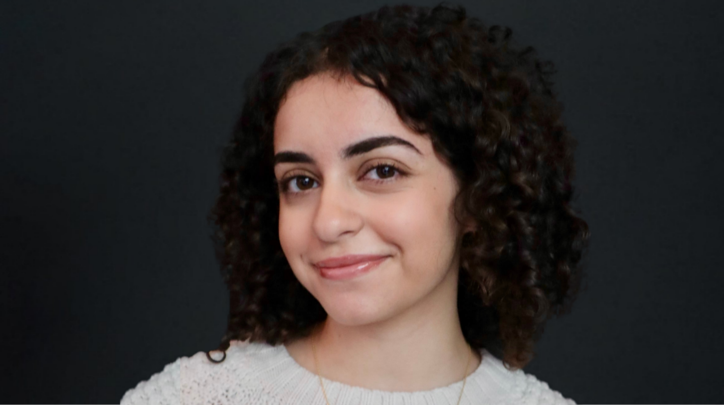 Portrait of a current Gannon Scholar with short curly dark hair, smiling, wearing a light-colored top, posed against a dark background.